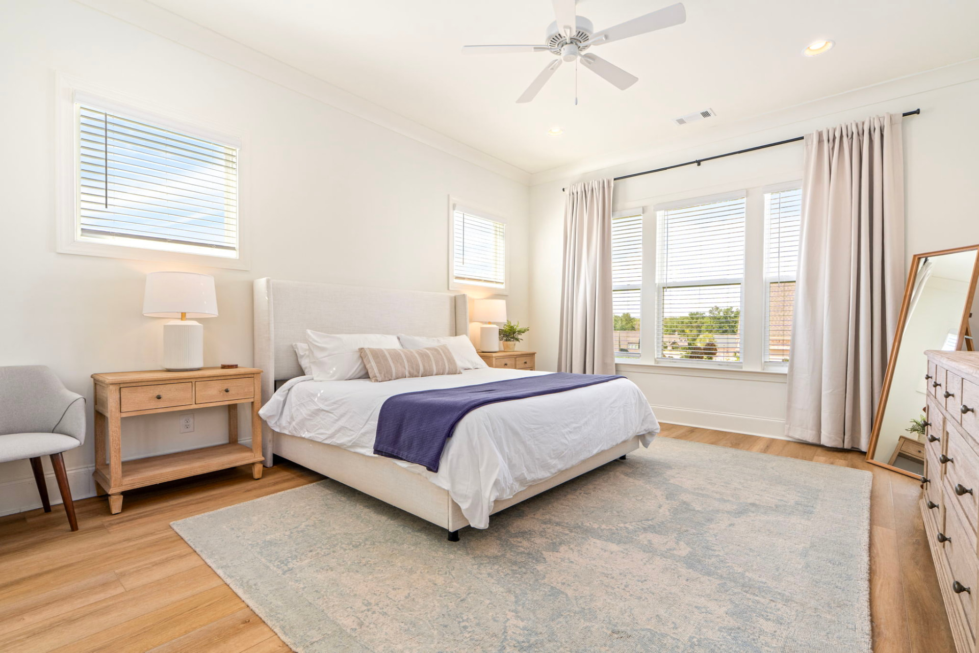 Primary suite with a king bed, white bedding and navy throw, wingback headboard and floor mirror