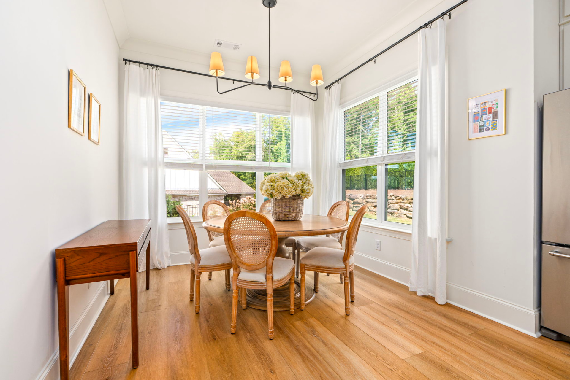 Dining area with a round wooden table, cane-back chairs and a black chandelier