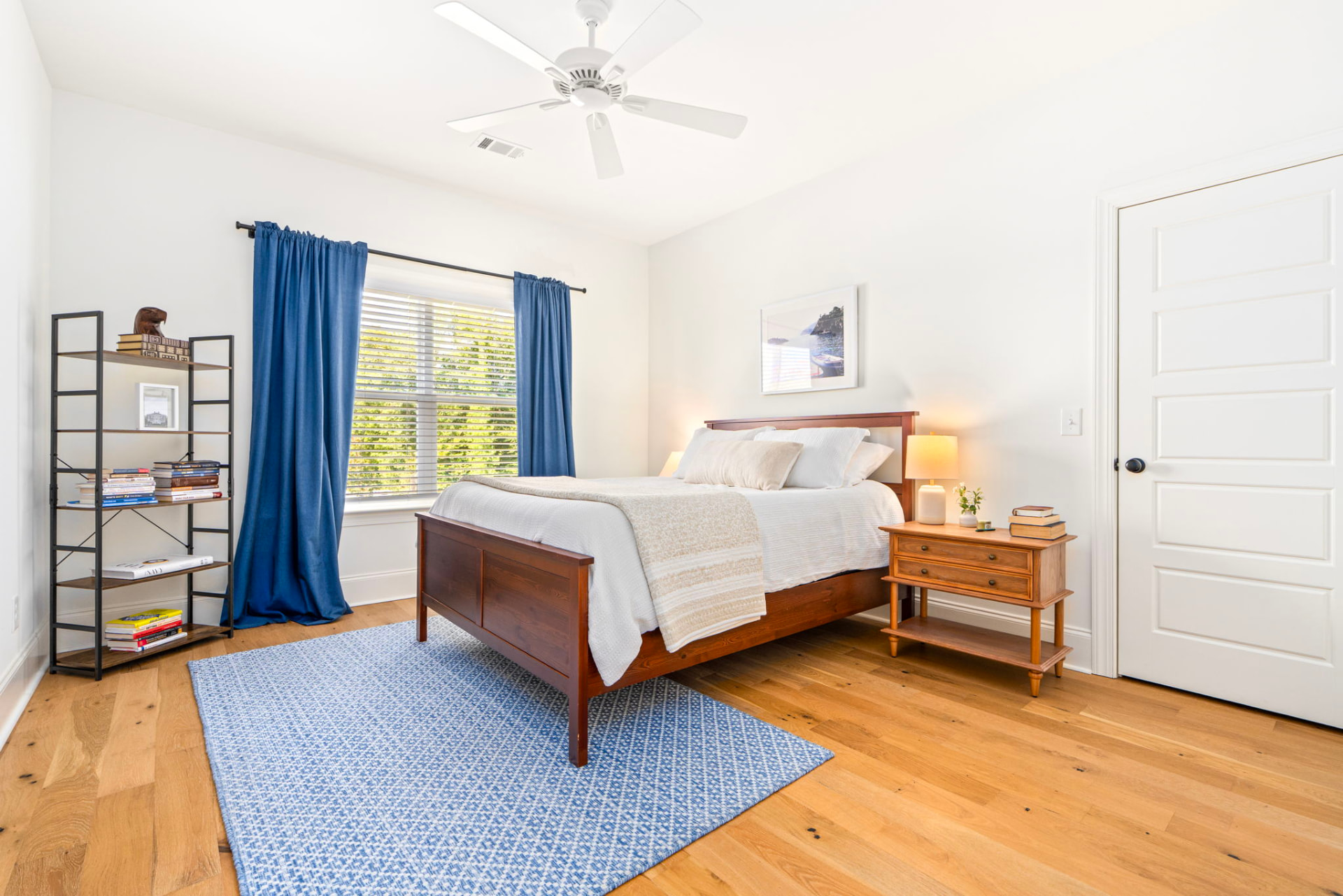 Upstairs guest bedroom with a queen bed, navy blue curtains, ceiling fan and hardwood floors