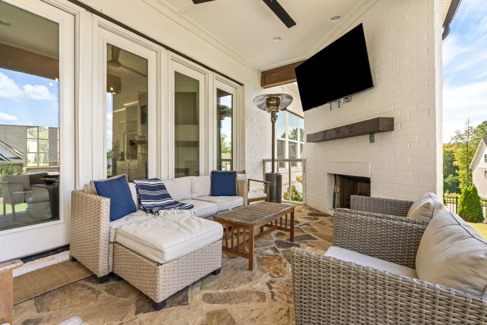 Covered back porch with a brick fireplace, mounted TV, patio heater and wicker lounge seating