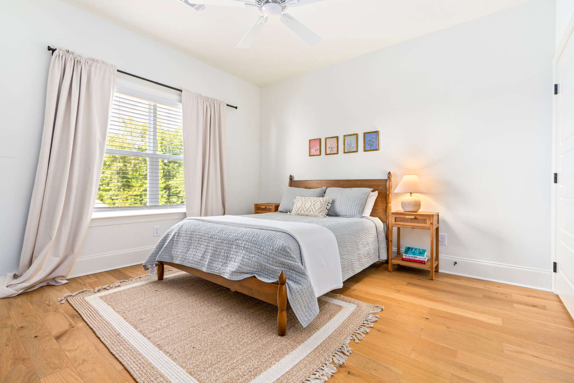 Guest bedroom with a queen bed, wooden headboard, gray quilted bedding, botanical prints and a rattan nightstand