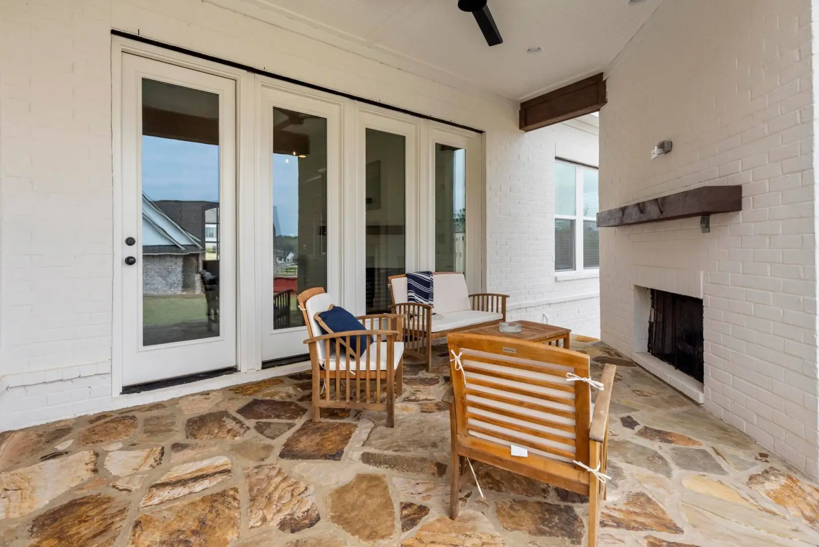 Covered porch with a brick fireplace, teak chairs and a stone patio