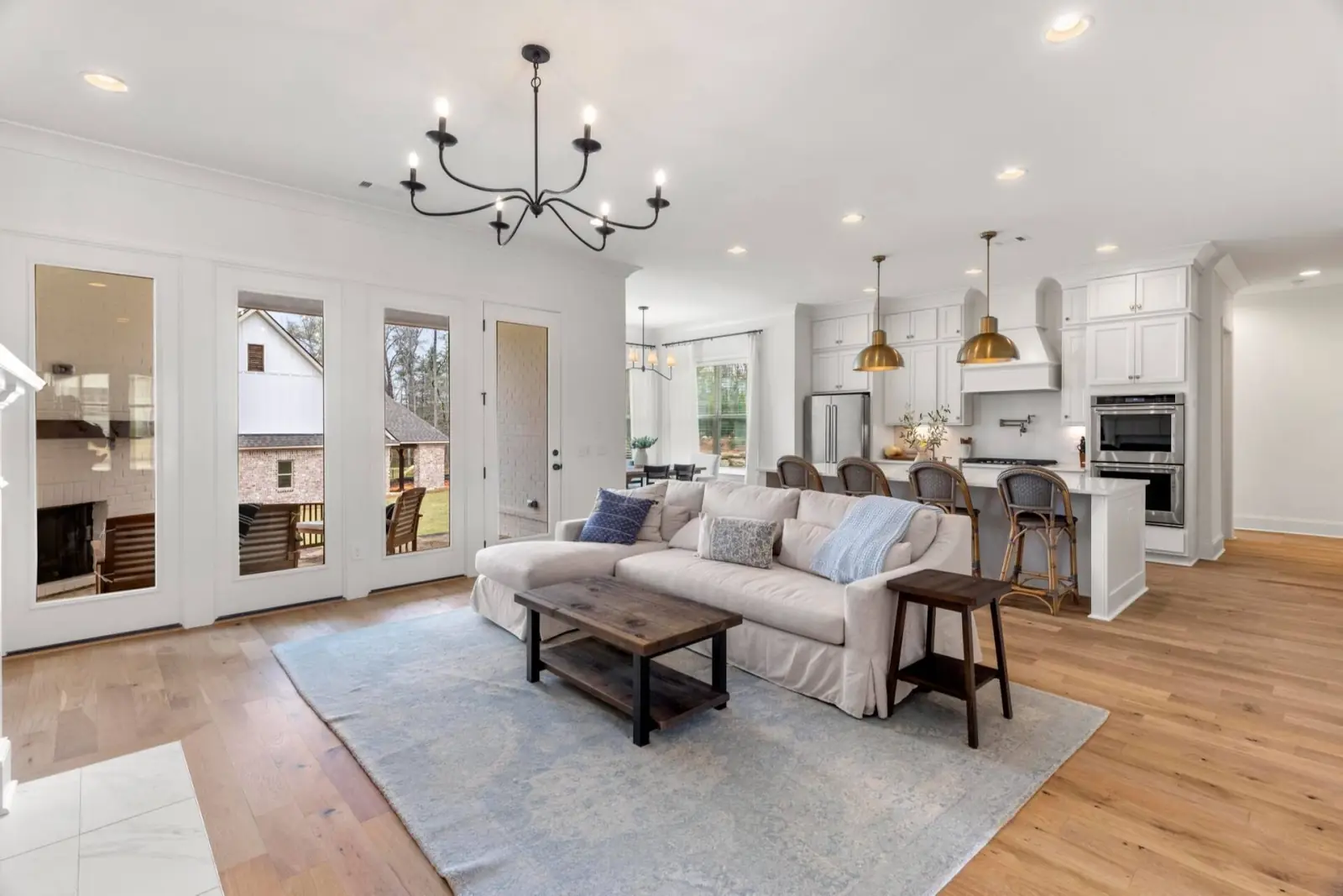 Great room with slipcovered sofa and iron chandelier open to the kitchen and dining area